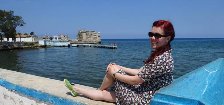 Person sits with legs crossed on a wall that overlooks a bay.