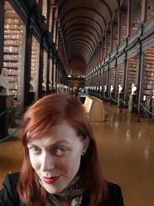 Person stands in front of a long hall that has a vaulted Cathedral ceiling and is lined with rows of books.