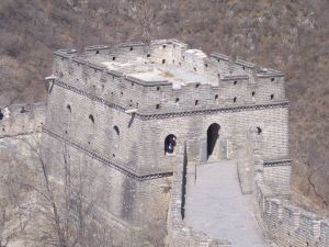 Person sits inside the window of a square stone structure at a juncture of the Great Wall.